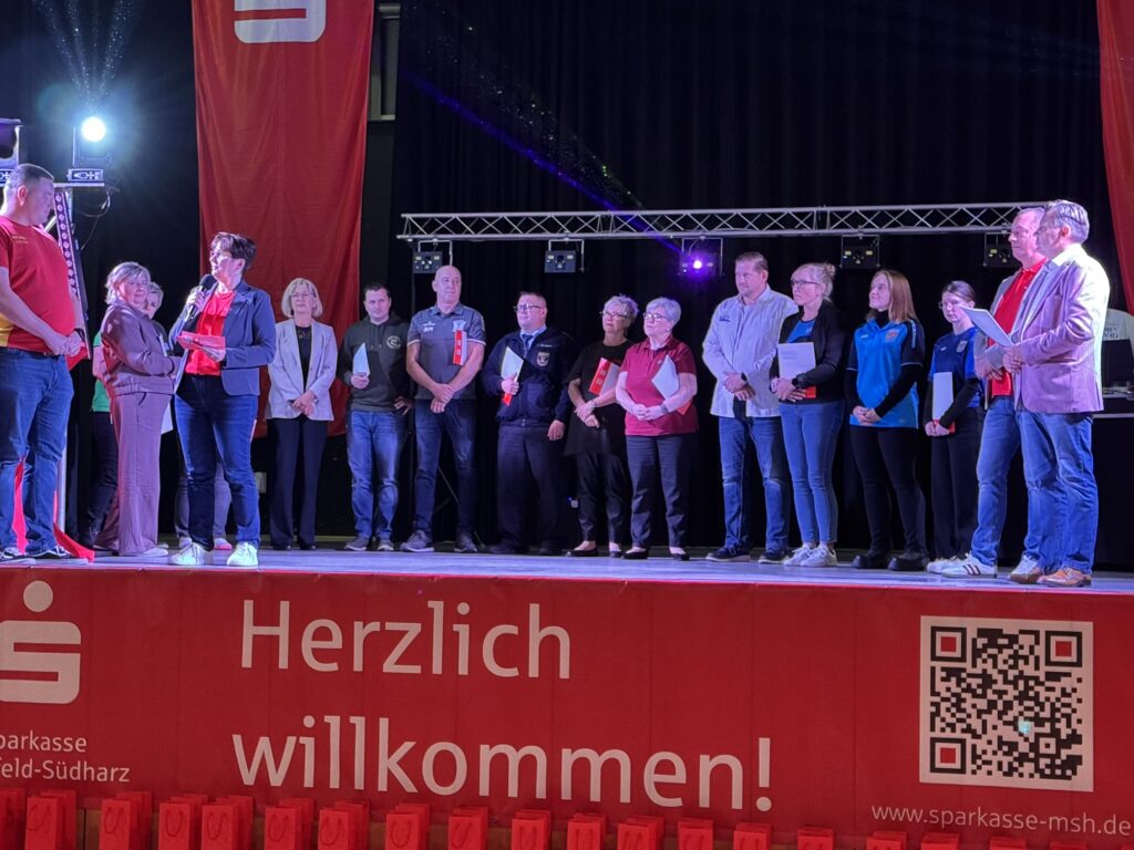 Vertreterinnen und Vertreter mehrerer geförderter Vereine stehen mit ihren Unterlagen auf der Bühne